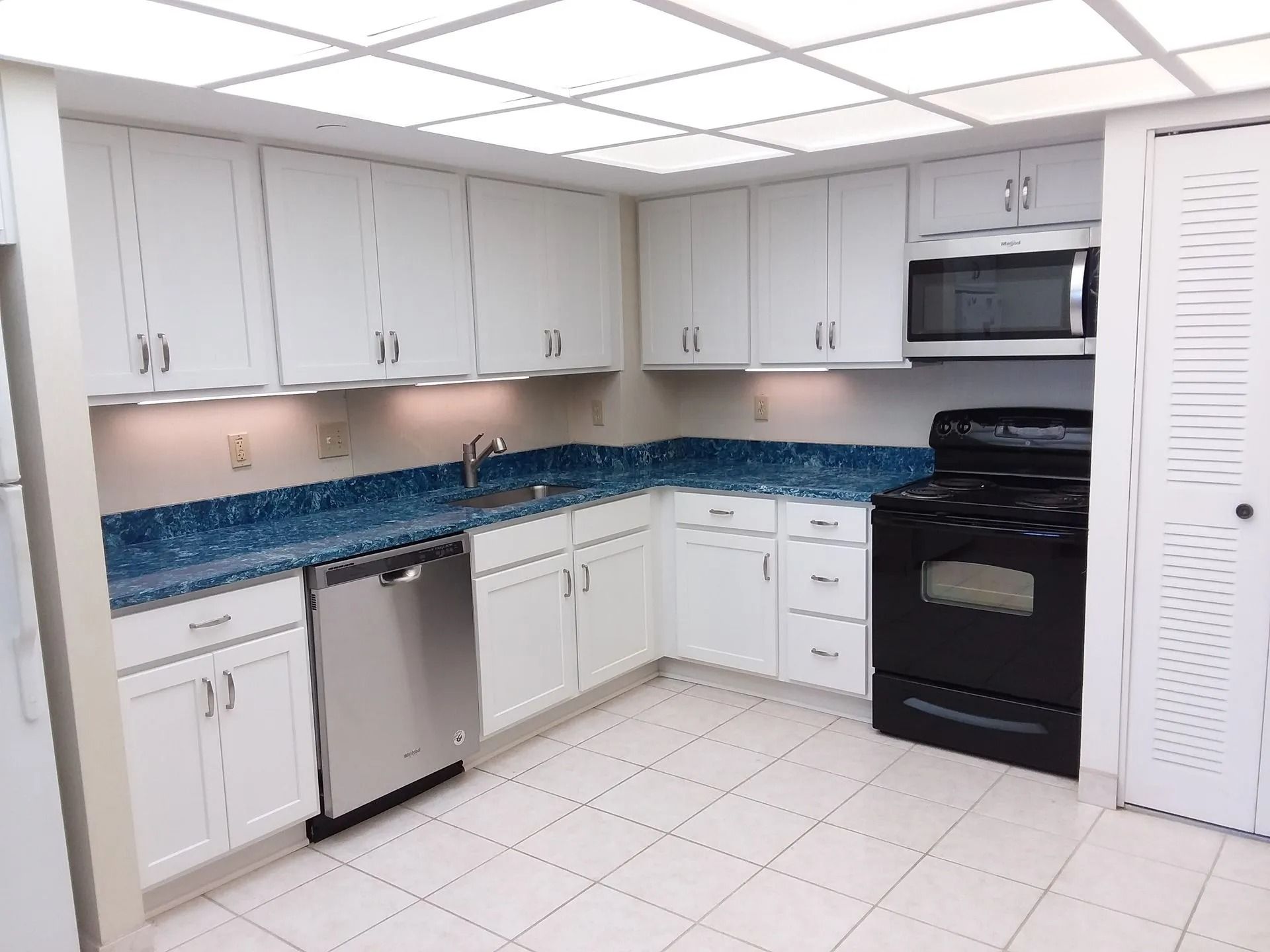 Bright kitchen with gray cabinets, blue tile backsplash, white floor, and black appliances