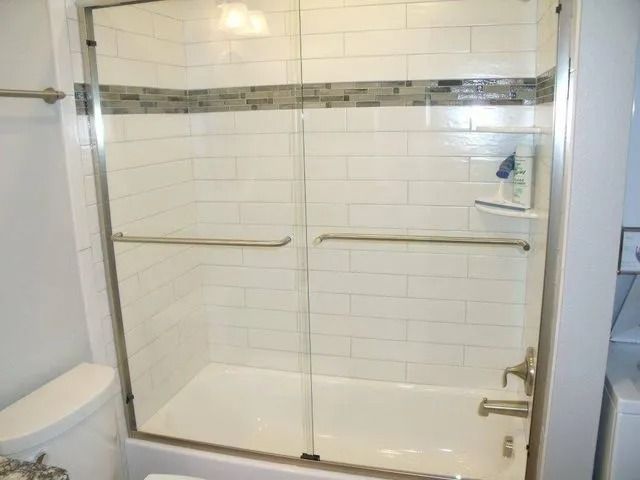 White tiled bathroom with a glass-enclosed walk-in shower and chrome grab bars