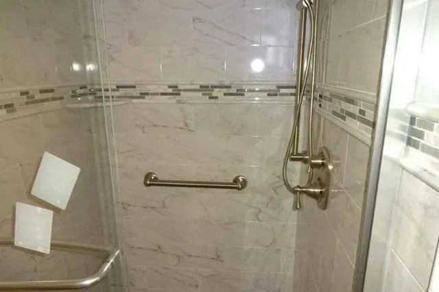 Tiled bathroom shower with glass door, metal grab bars, and handheld showerhead