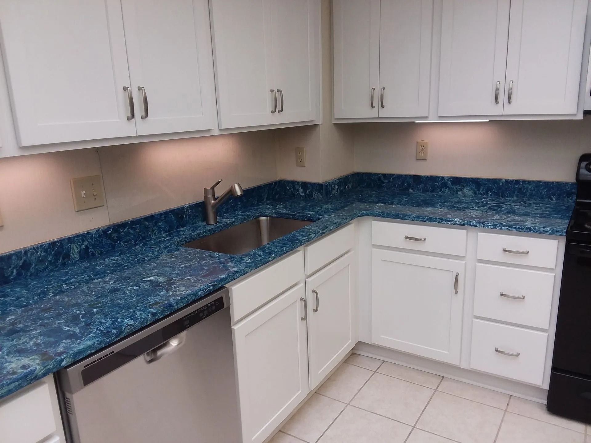 White kitchen with blue countertops, stainless sink, and white cabinets and drawers.