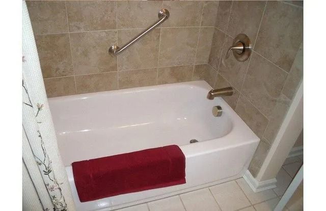 Bathroom tub with beige tile walls, grab bar, and a red towel draped over the edge