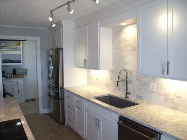 Modern white kitchen with marble countertops, stainless fridge, and under-cabinet lighting
