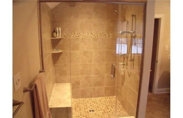 Walk-in shower with tan tile walls, glass door, built-in bench, and handheld showerhead