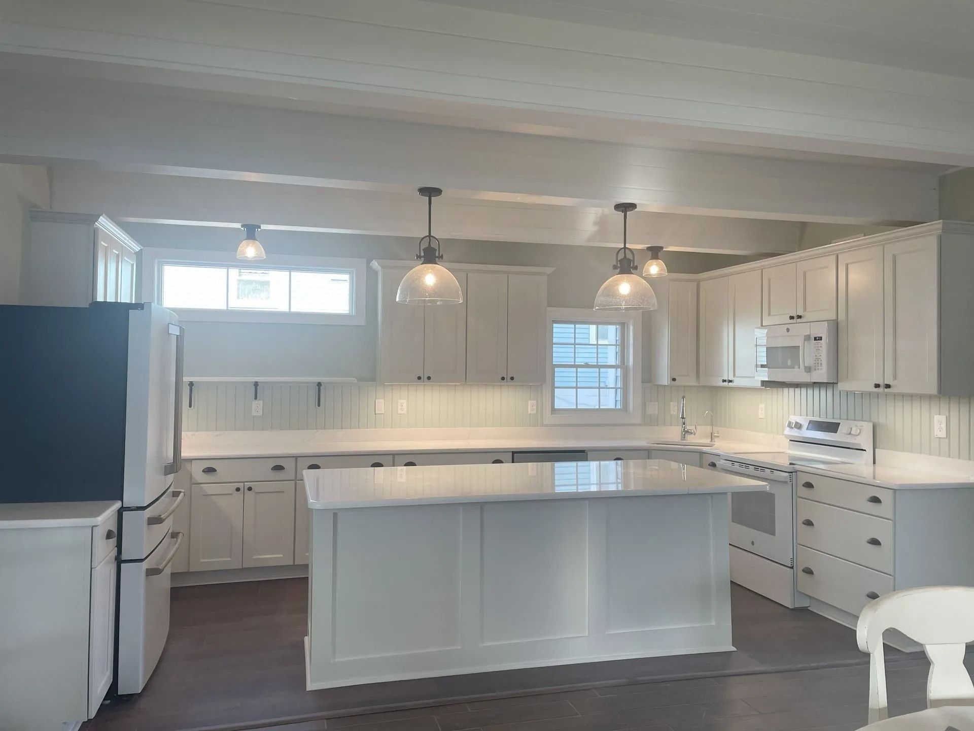 Bright white kitchen with island, pendant lights, gray floor, and large refrigerator.