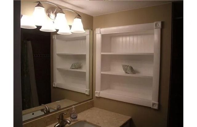 Bathroom mirror with vanity lights and two white wall shelves, one holding a small decorative item.