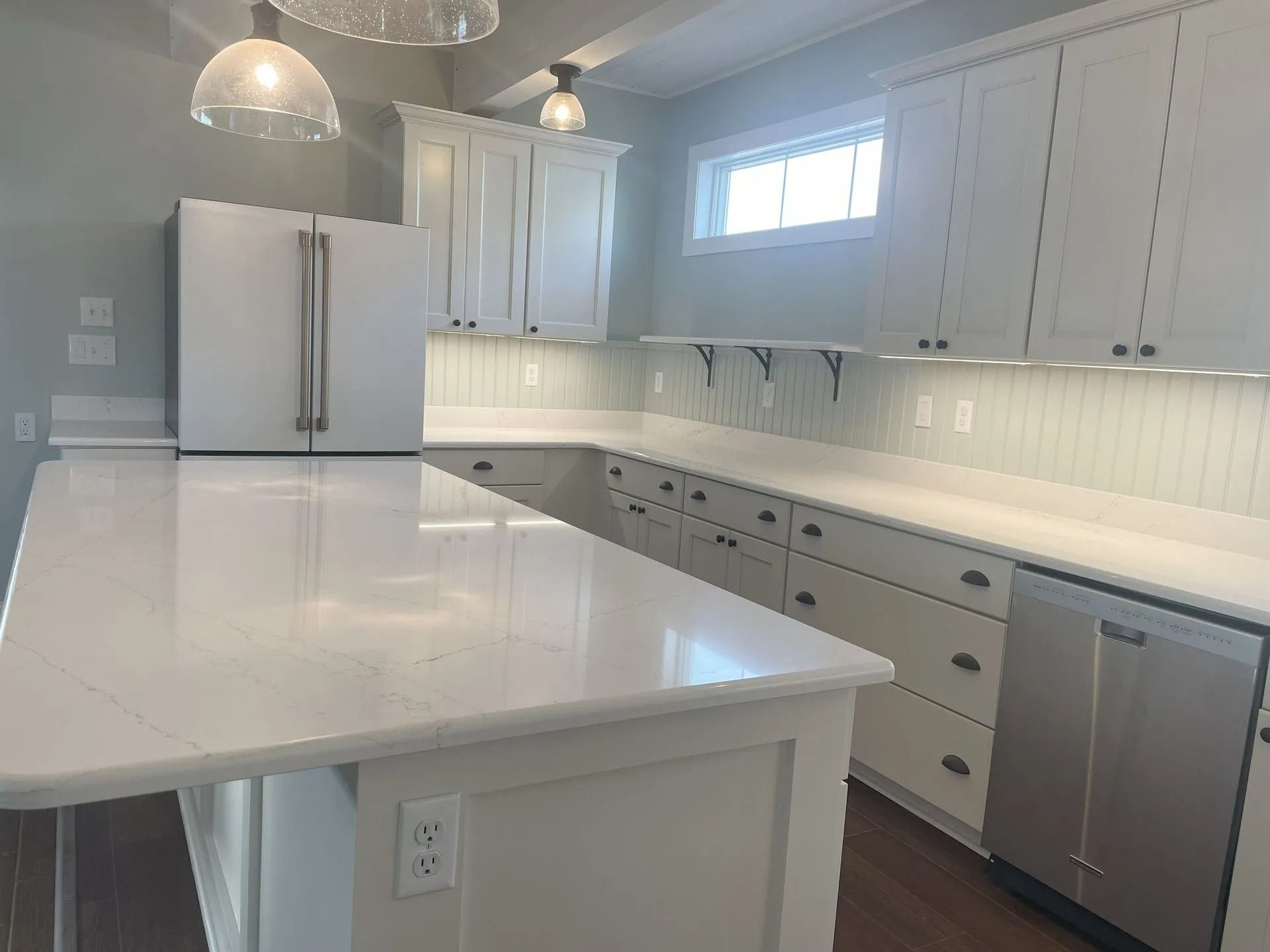 Bright white modern kitchen with large island, stainless appliances, and pendant lights