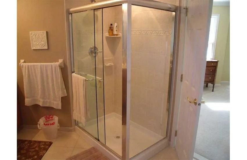 Bathroom with glass shower enclosure, towels, and a doorway to a carpeted room.