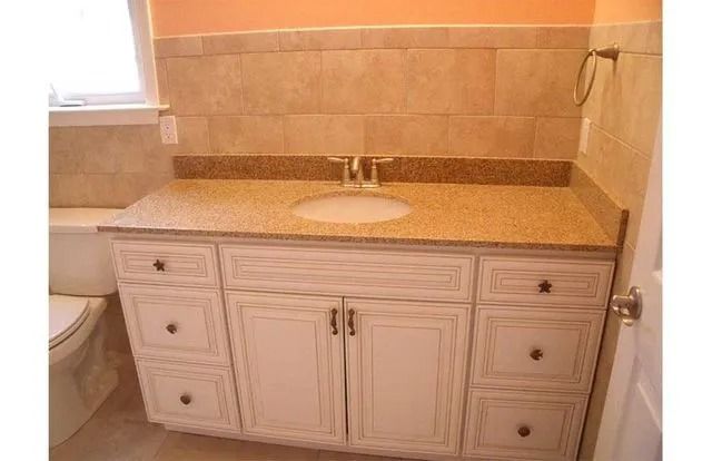 Bathroom vanity with white cabinets, granite countertop, and round sink under a beige tiled backsplash