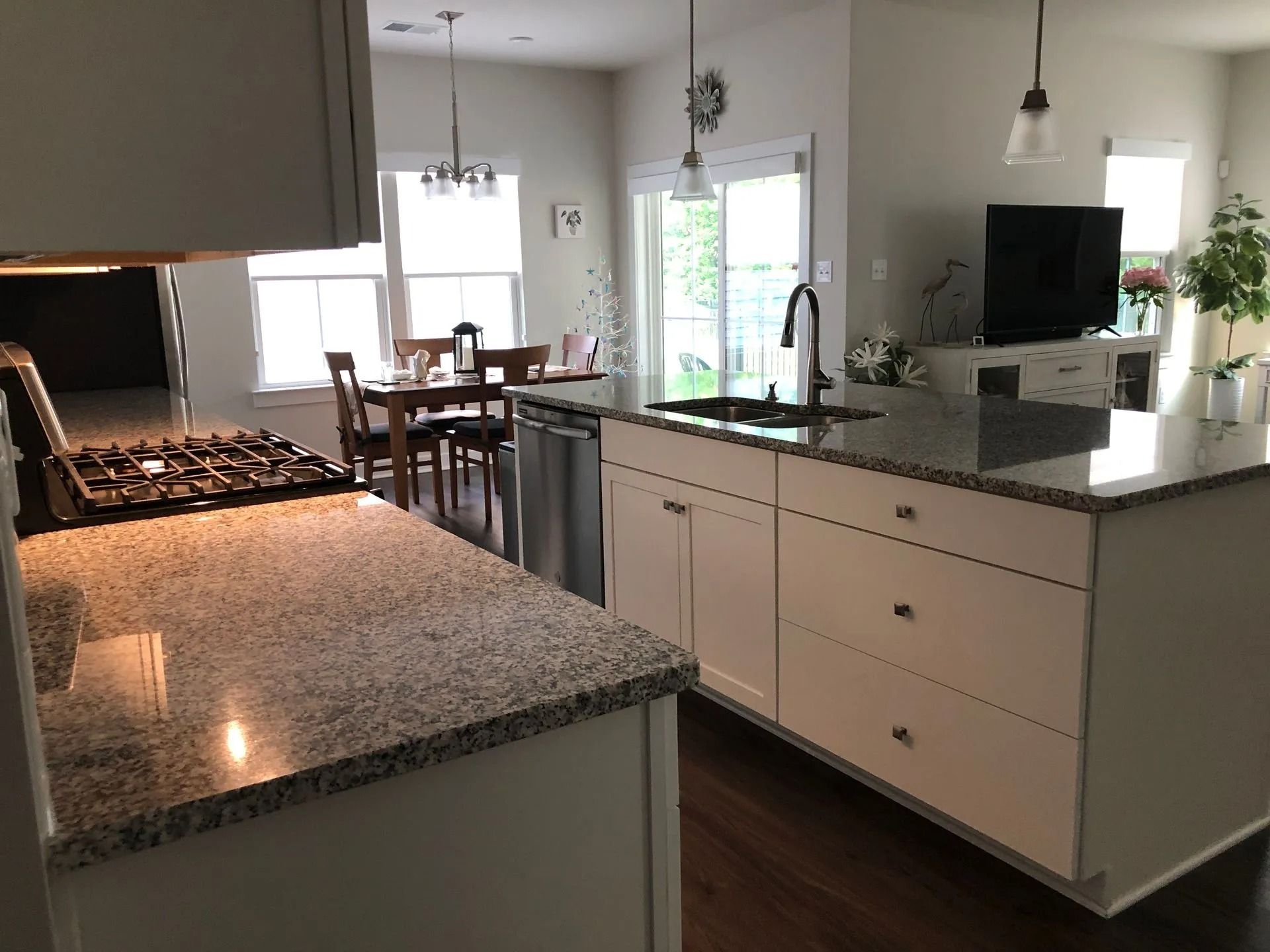 Modern kitchen with granite island, white cabinets, dining table, and sliding glass door to the patio.