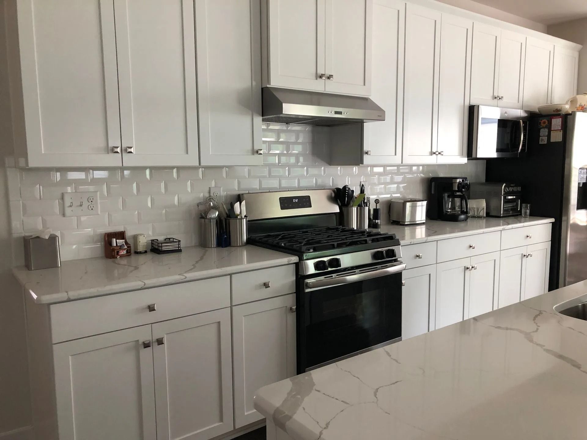 Modern white kitchen with cabinets, subway tile backsplash, black stove, and marble-patterned island countertop