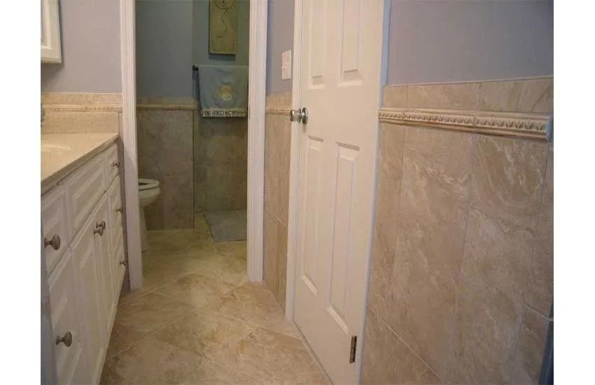 Narrow bathroom hallway with beige tile, white doors, and a vanity cabinet on the left.