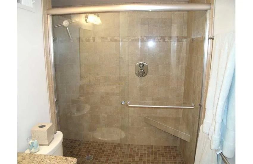 Glass-enclosed shower with beige tile walls, chrome grab bar, and a soap dish in a bathroom.