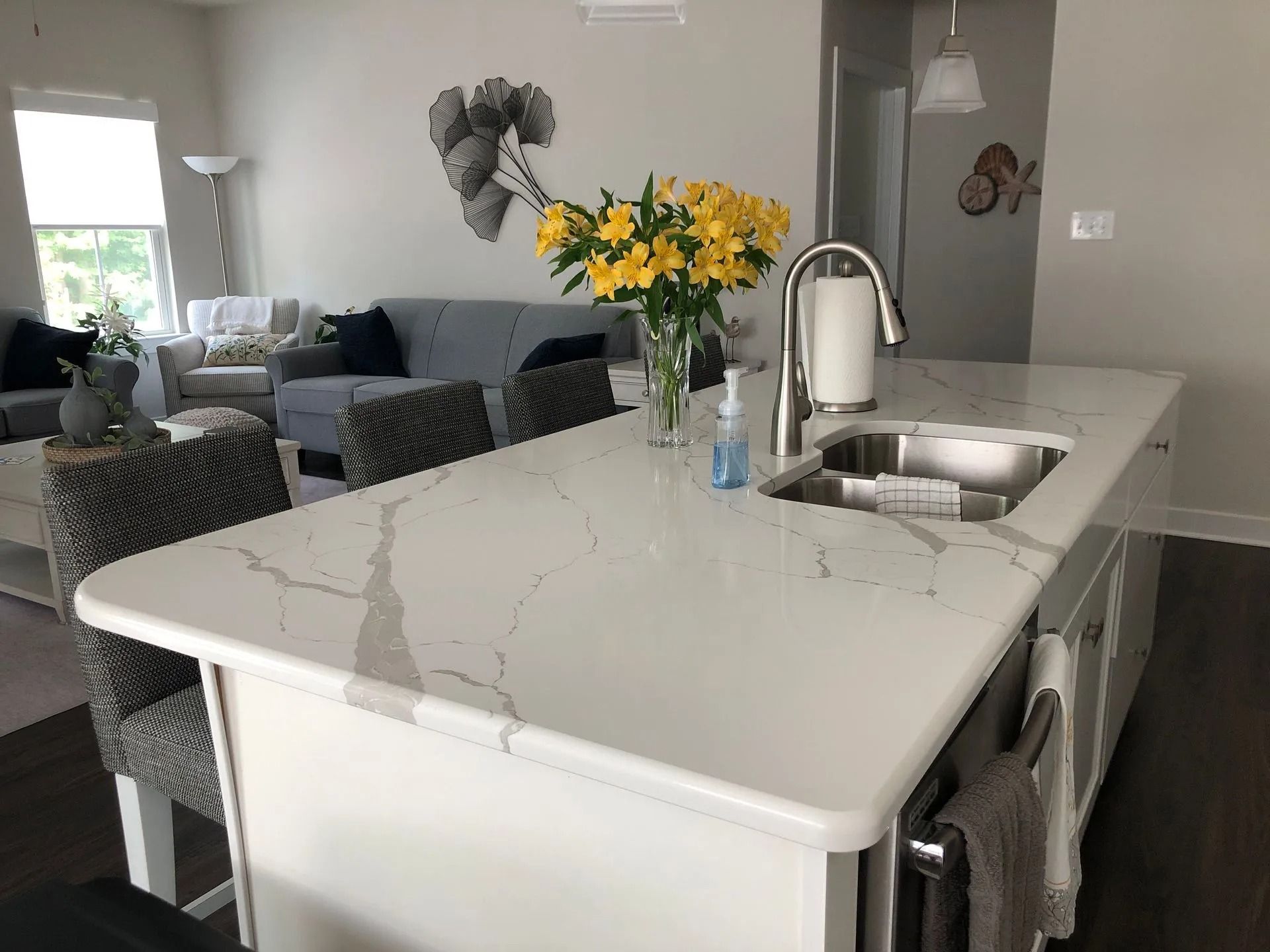 Modern kitchen island with marble countertop, sink, flowers, and adjacent gray living room seating