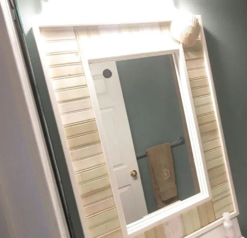 Bathroom mirror above sink with beige striped wallpaper and a towel hanging on the door