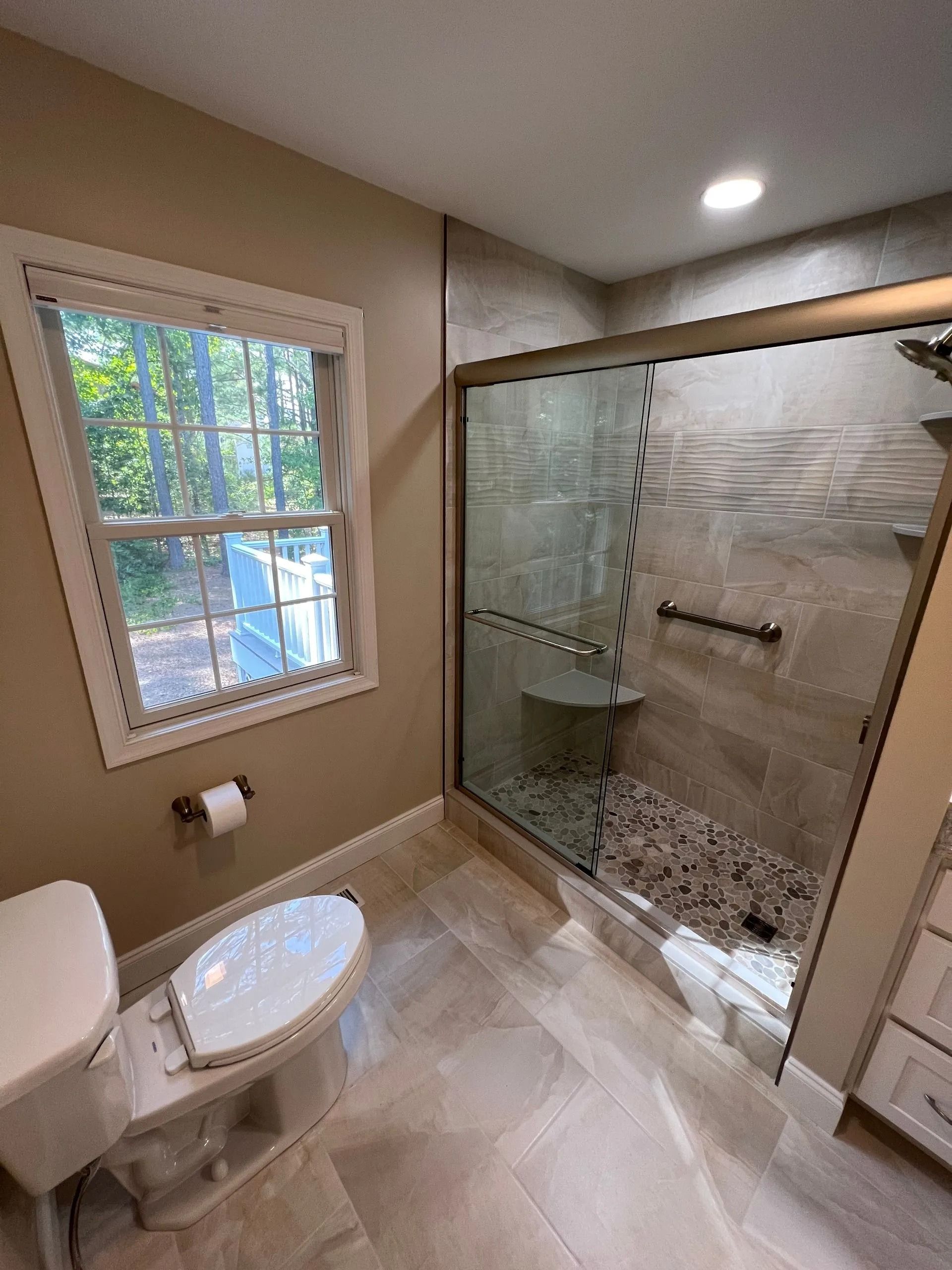 Modern bathroom with walk-in glass shower, toilet, window, and beige tile floor.
