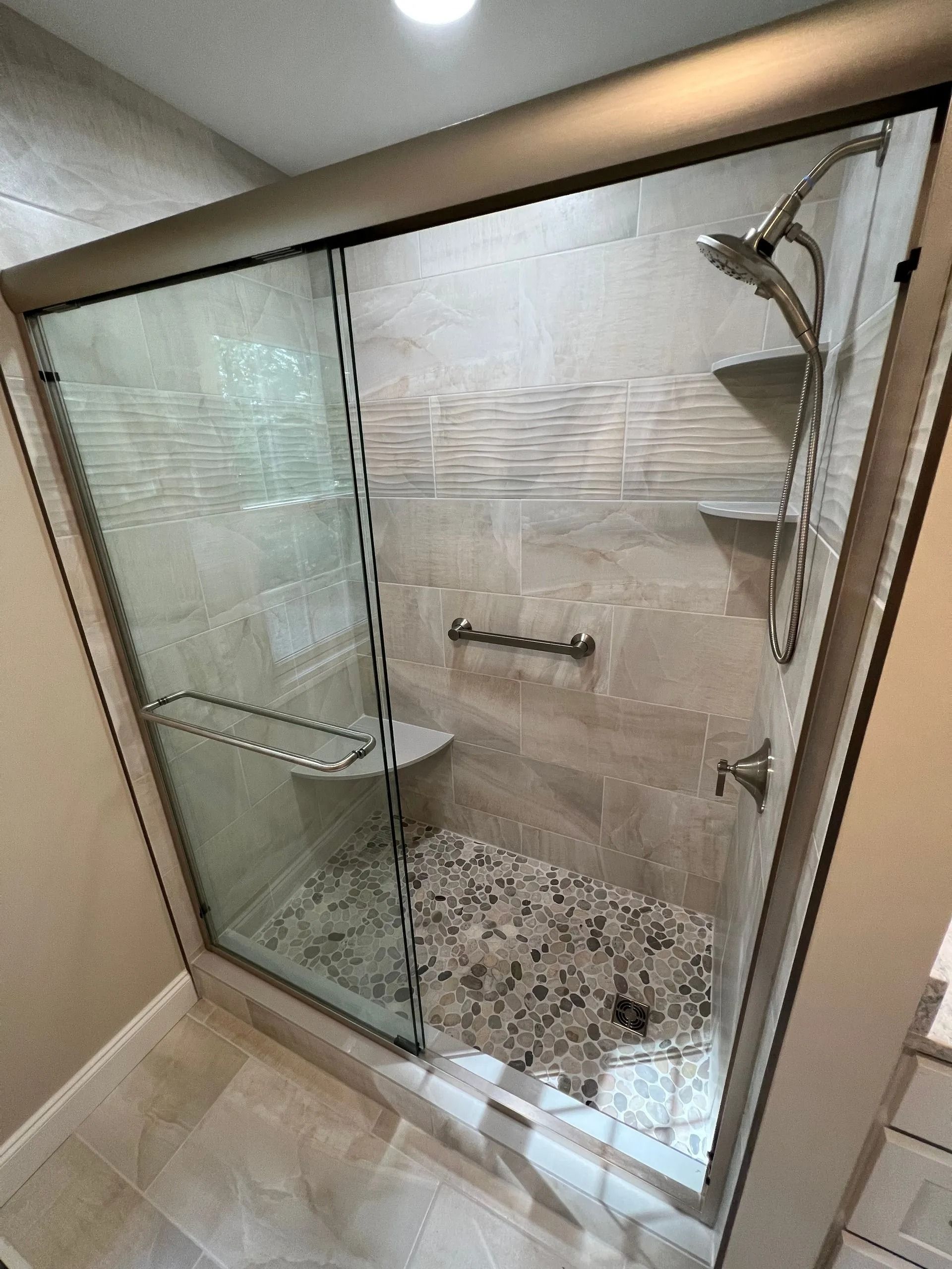 Glass walk-in shower with chrome fixtures, pebble floor, and frosted tile wall.