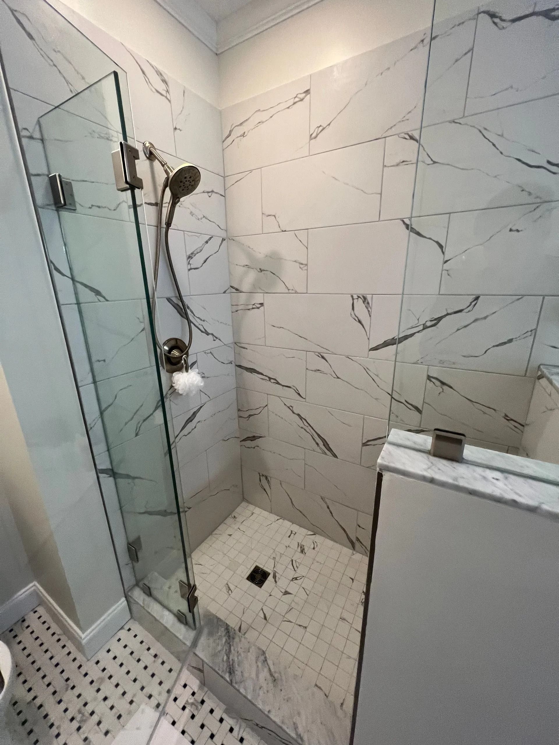 Modern tiled shower with glass door, handheld showerhead, and built-in shelf