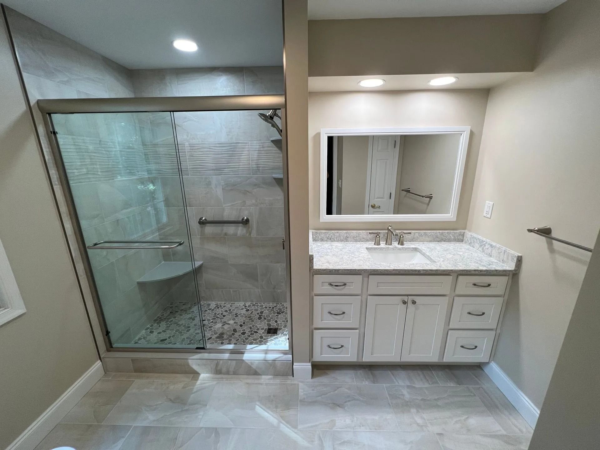 Modern bathroom with glass shower, large mirror, and white vanity with granite countertop.