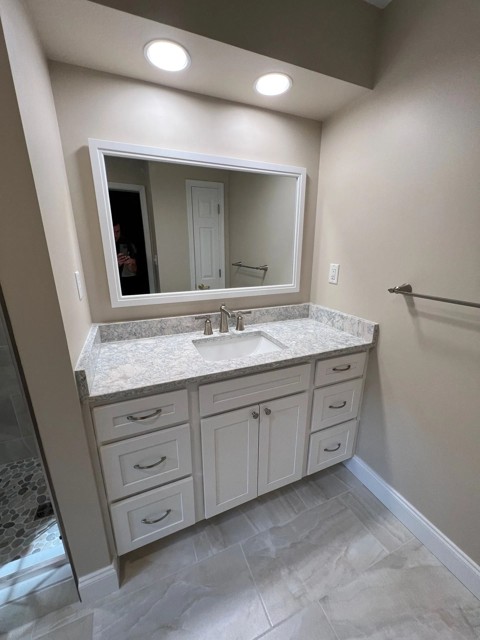 Bathroom vanity with large mirror, white cabinets, marble countertop, and wall towel bar.