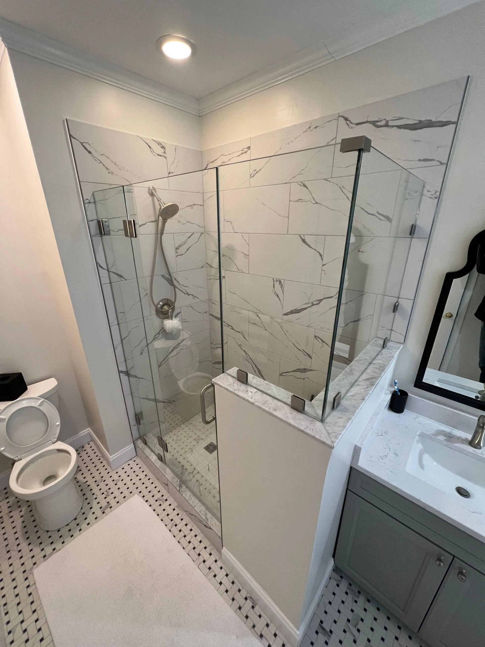 Small modern bathroom with walk-in glass shower, white tile, toilet, and vanity sink.