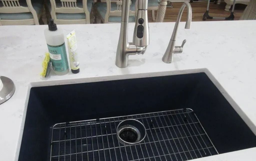Modern kitchen sink with black basin, chrome faucet, soap dispenser, and cleaning items on a white countertop