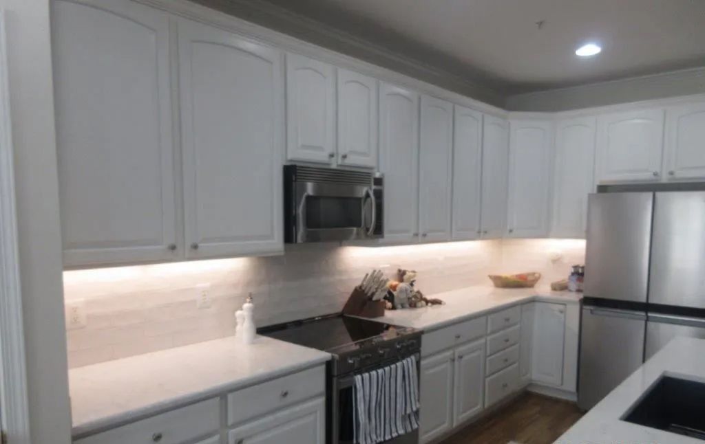 Modern white kitchen with stainless steel appliances, under-cabinet lighting, and dark countertops