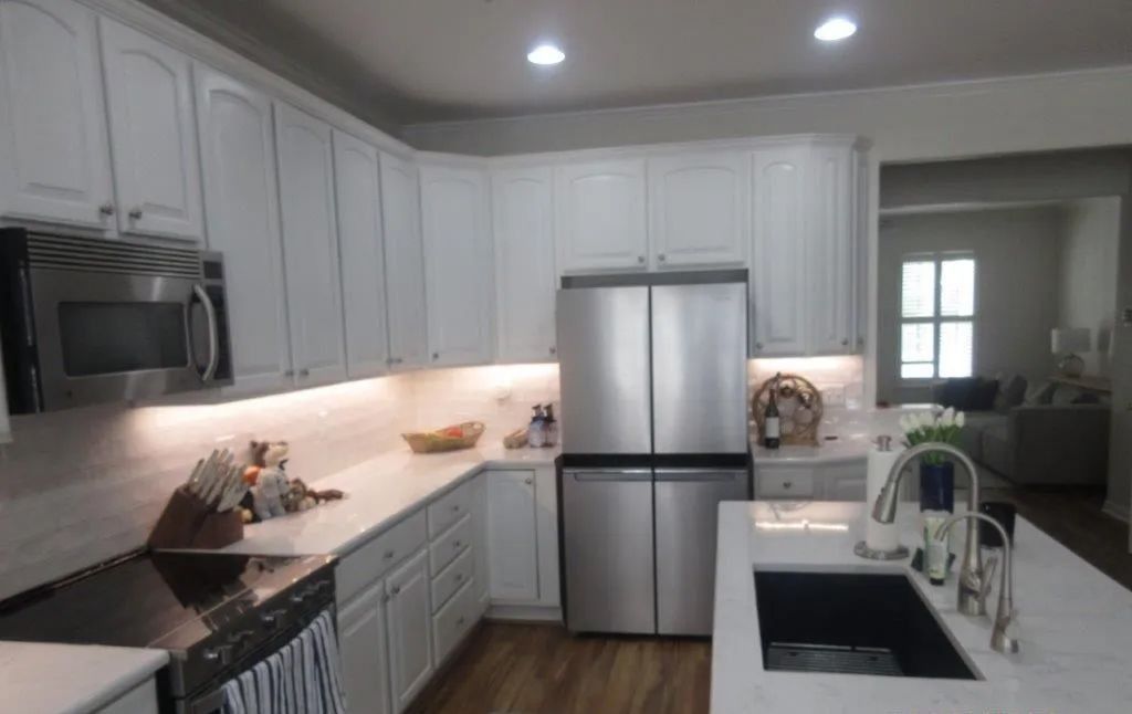 Modern white kitchen with stainless appliances, island sink, and wood floors