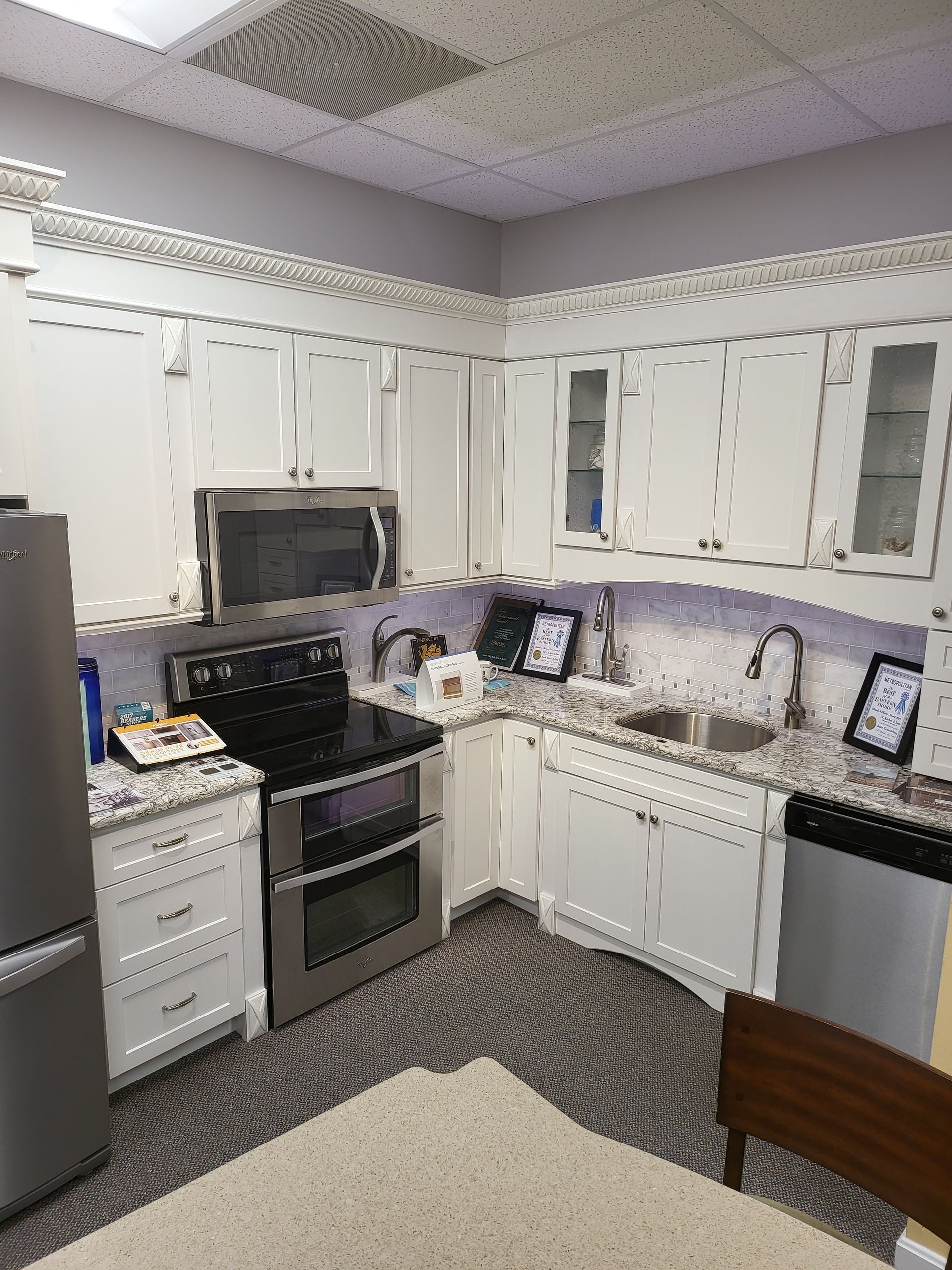 Compact white kitchen with black stove, countertop, and cabinets under a patterned ceiling