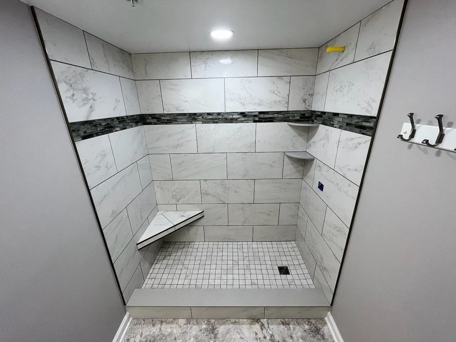 Tiled walk-in shower with bench, corner shelf, and wall hooks in a small bathroom