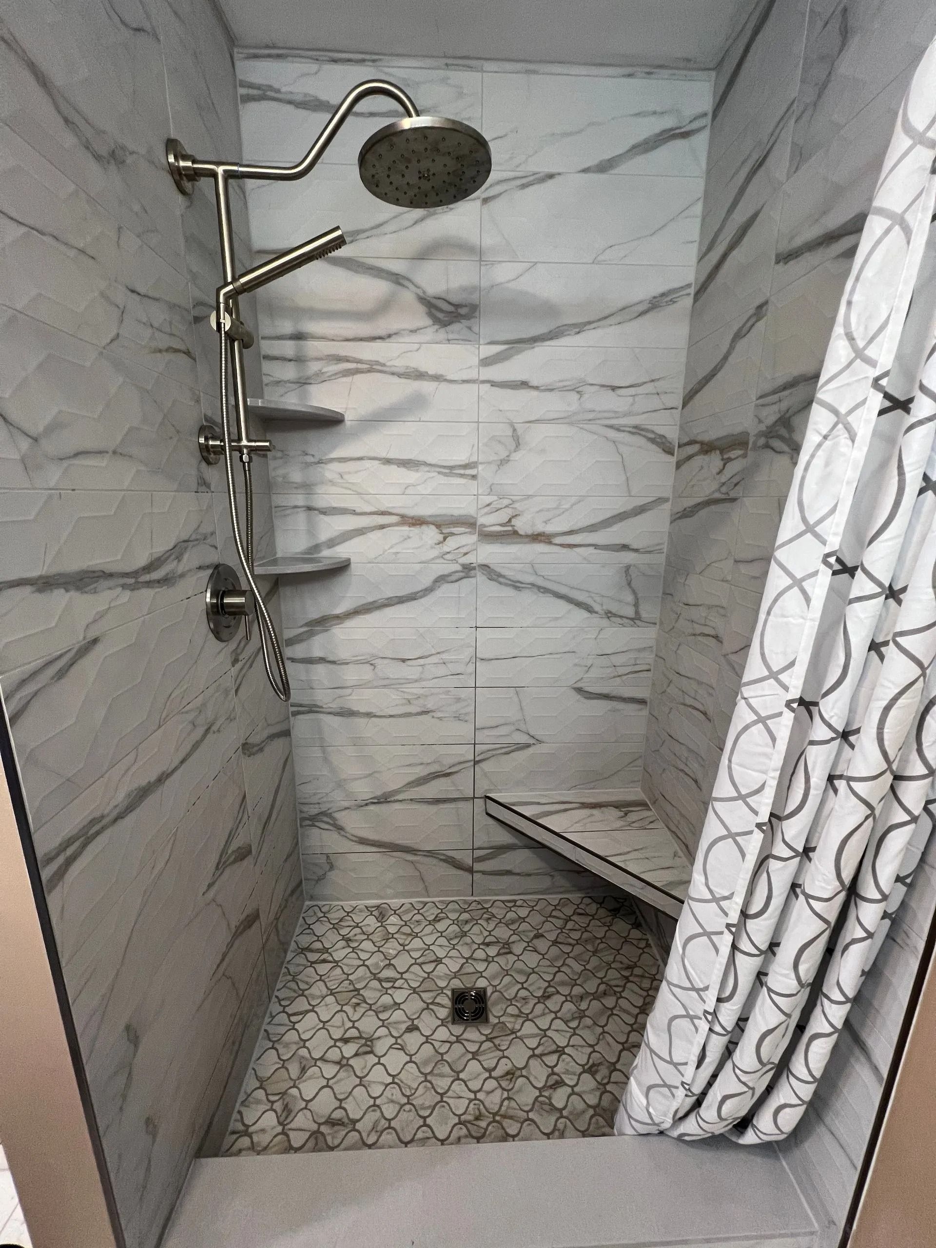 Small tiled shower with marble-look walls, rain showerhead, built-in bench, and a curtain on the right.