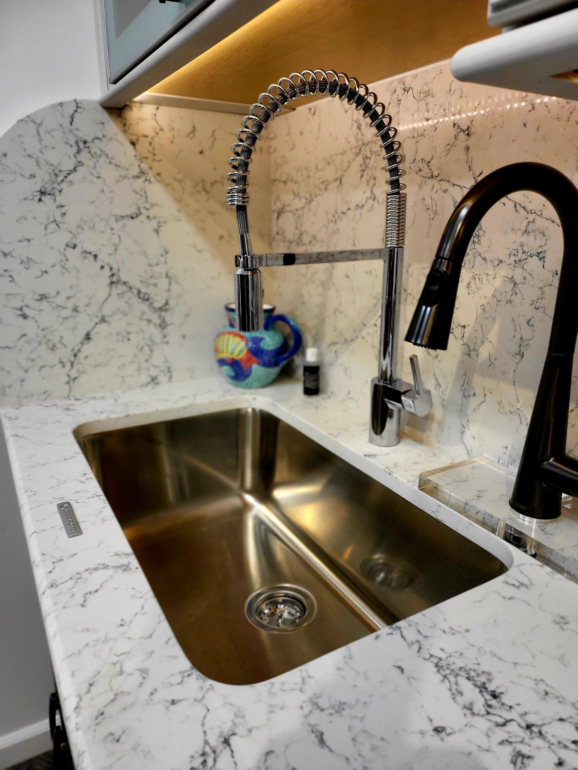 Kitchen sink with two black faucets and a blue sponge hanging on a chrome sprayer.