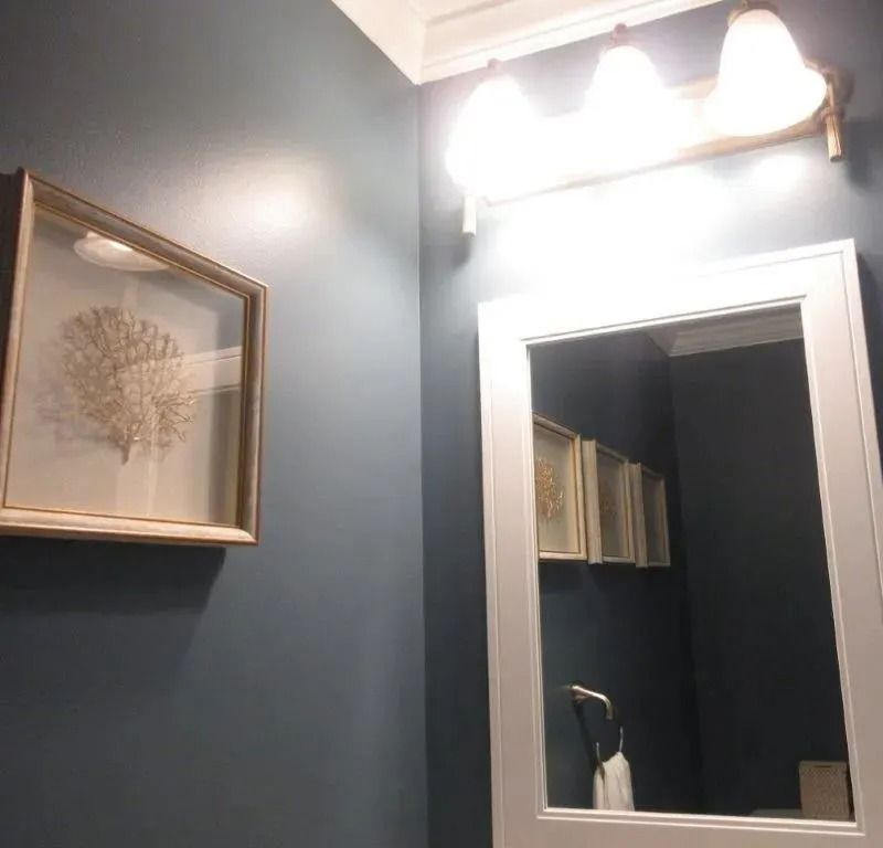 Bathroom wall with framed art, mirror, and bright vanity light above a sink.