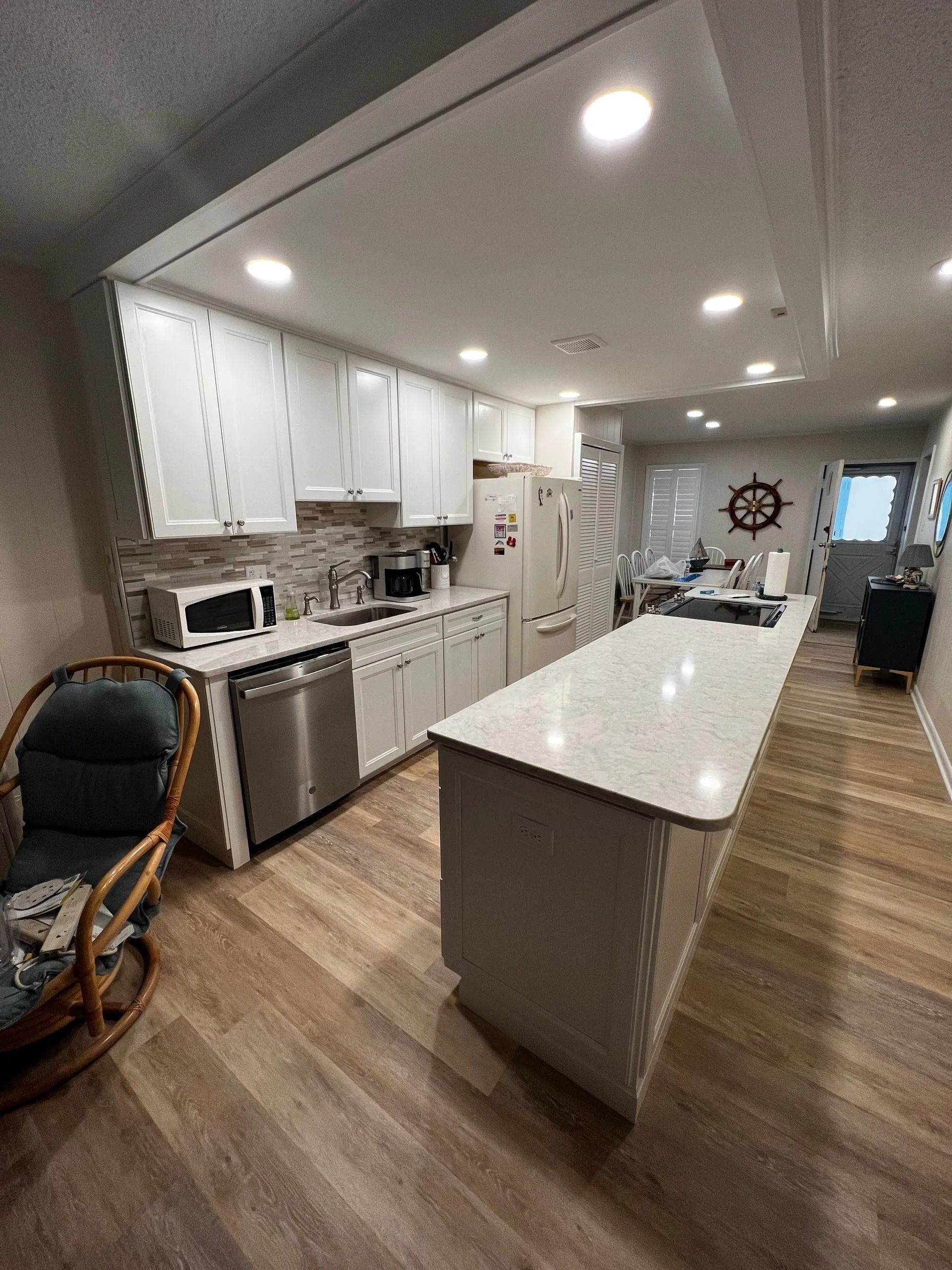 Modern white kitchen with island, wood floors, stainless appliances, and recessed ceiling lights