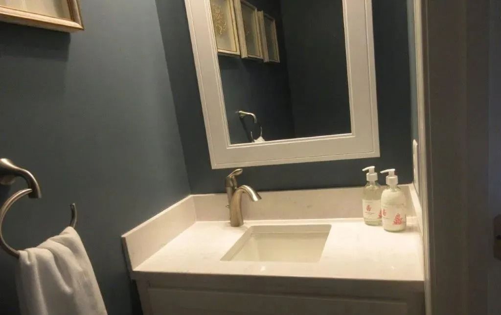 Small modern bathroom vanity with white sink, mirror, towel ring, and soap dispensers on the counter