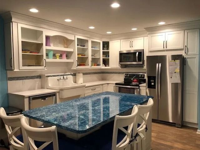 Modern white kitchen with blue island countertop, stainless steel appliances, and four chairs