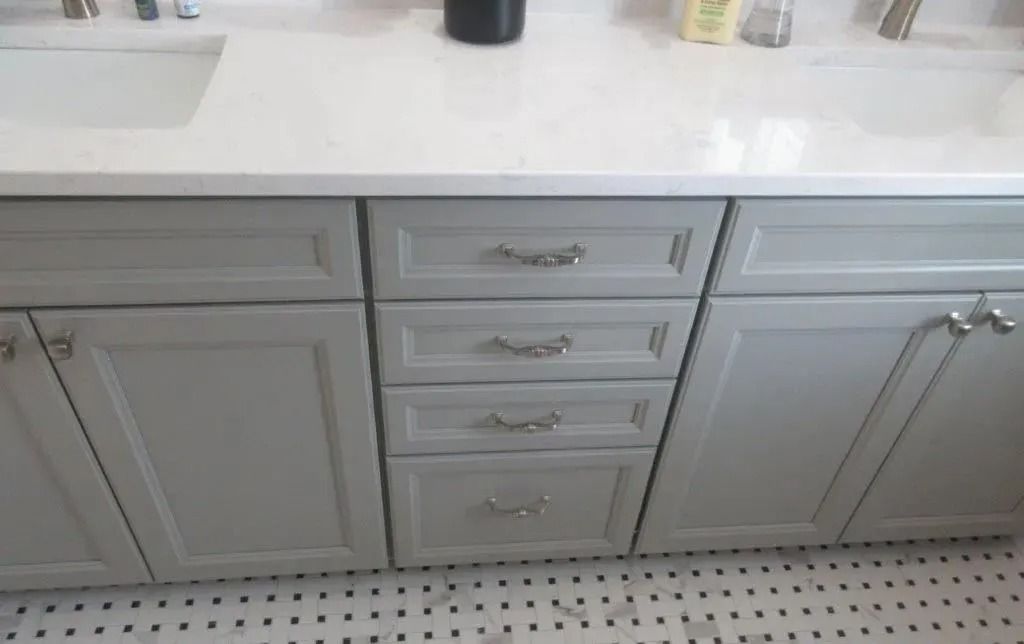 Gray bathroom vanity with drawers and cabinet doors beneath a white countertop and sink.