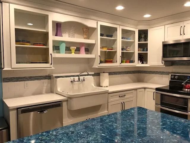 Bright white kitchen with open cabinets, stainless appliances, and a blue granite island countertop