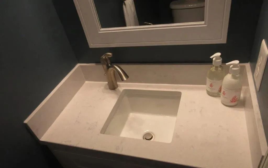 Bathroom vanity with white countertop sink, bronze faucet, and soap dispensers beside a mirror.