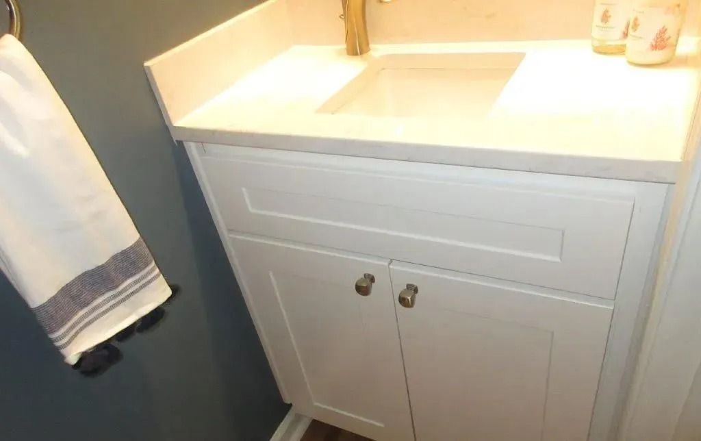 White bathroom vanity with sink, cabinet doors, and a towel hanging beside it.