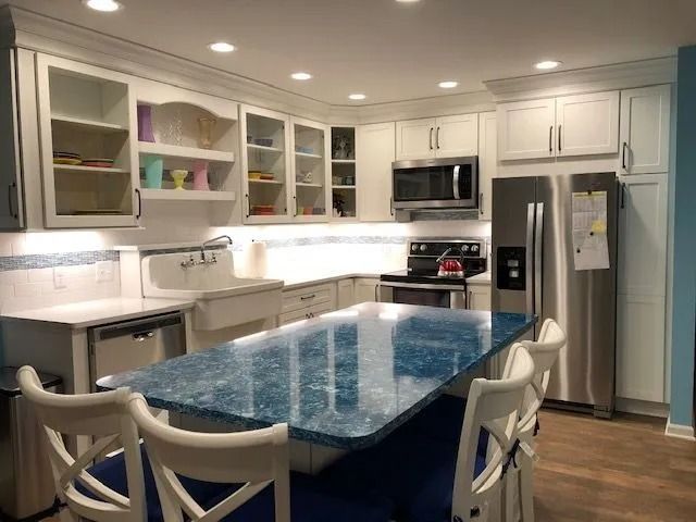Modern white kitchen with blue island countertop, stainless appliances, and bar stools