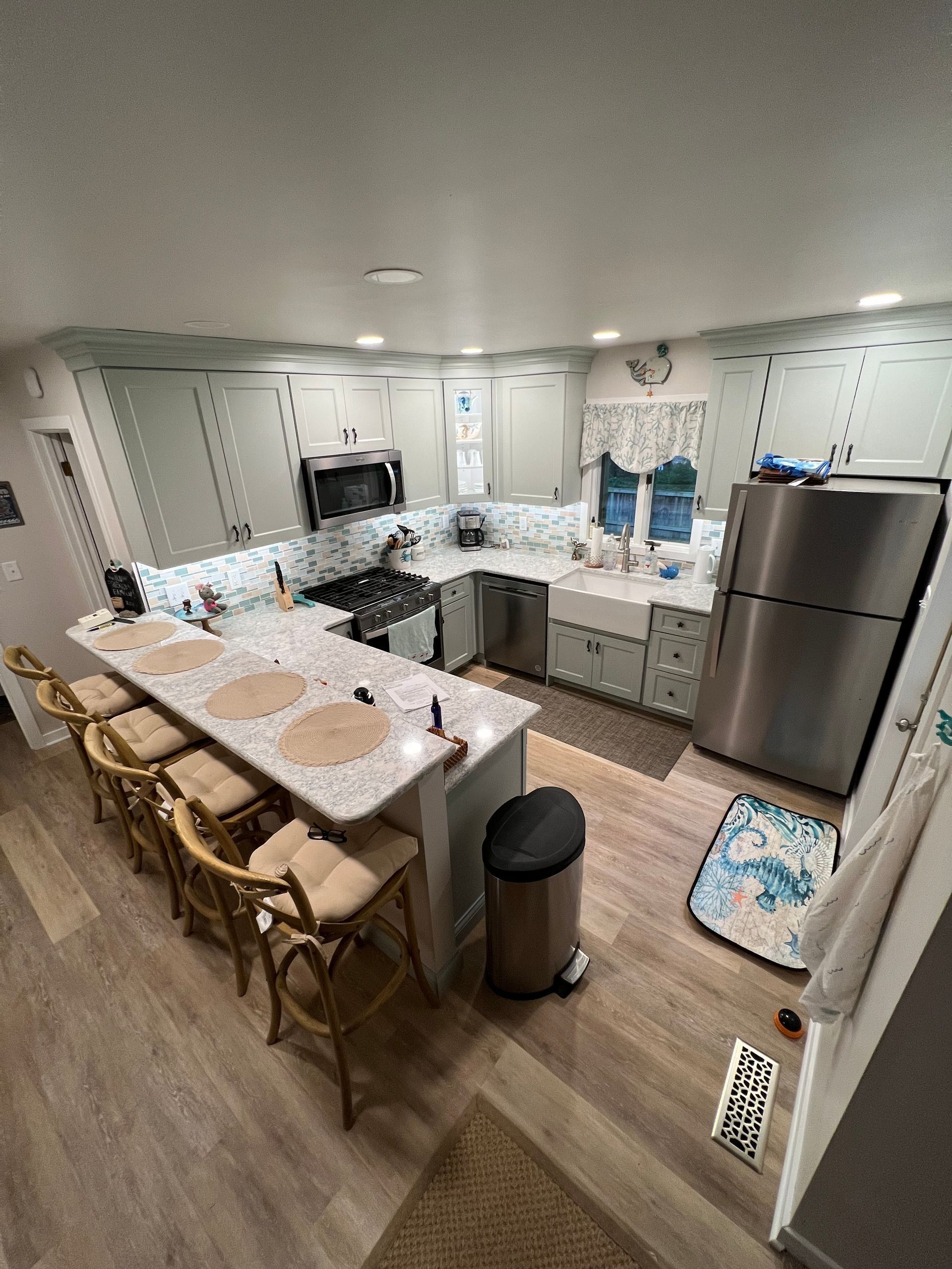 Bright kitchen with island seating, white cabinets, stainless fridge, and light countertops.