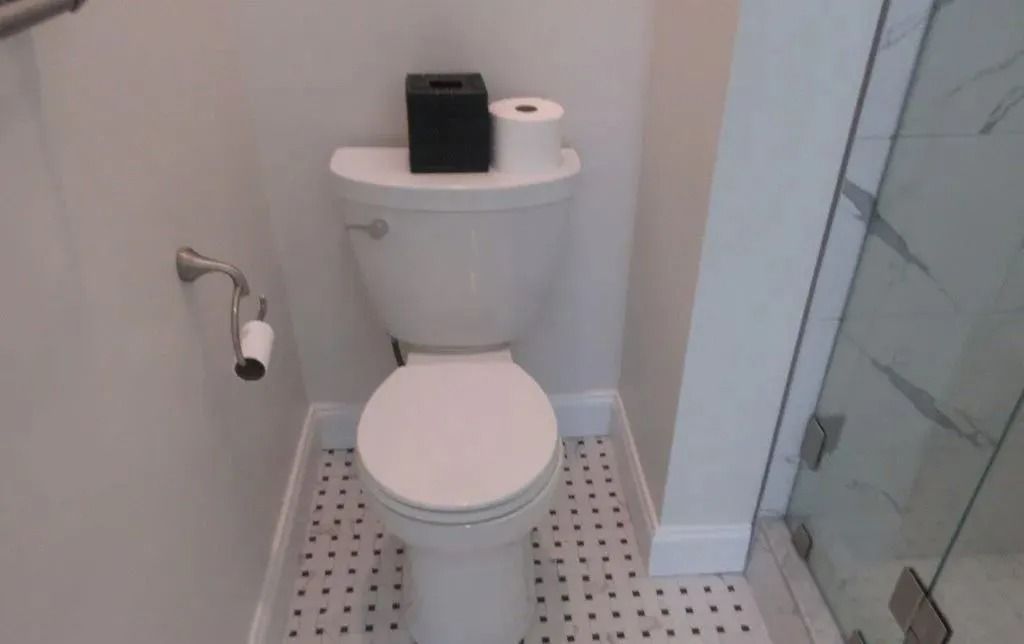 Small bathroom with a white toilet, toilet paper holder, and glass shower enclosure.