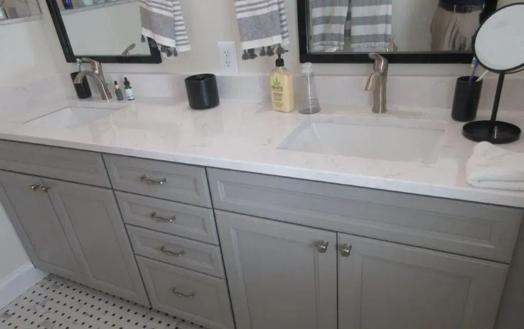 Gray bathroom vanity with white countertop, double sinks, mirror, and black-and-gold decor.