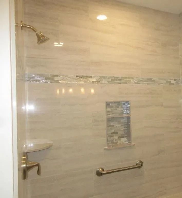 Tiled shower with brass fixtures, built-in shelf, and horizontal grab bar in a beige bathroom.