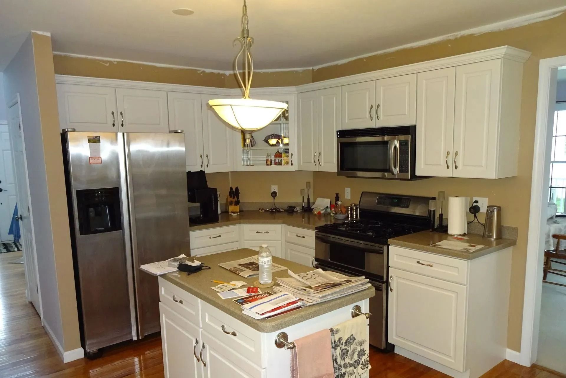 Bright white kitchen with stainless steel appliances and a central island under a hanging light.