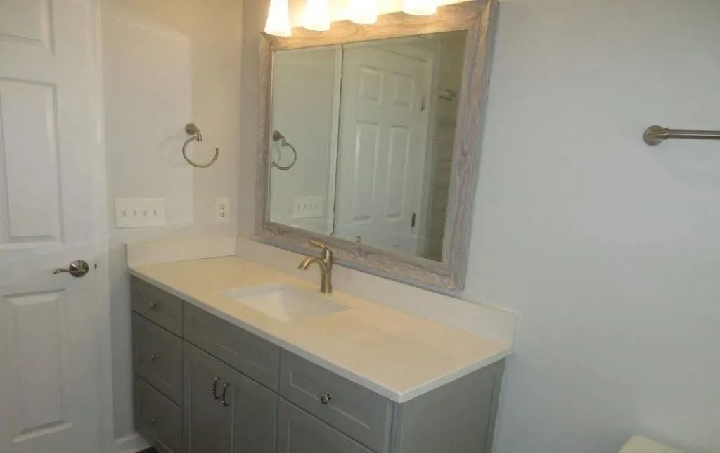 Bathroom vanity with sink, mirror, light fixtures, and gray cabinet against a white wall.