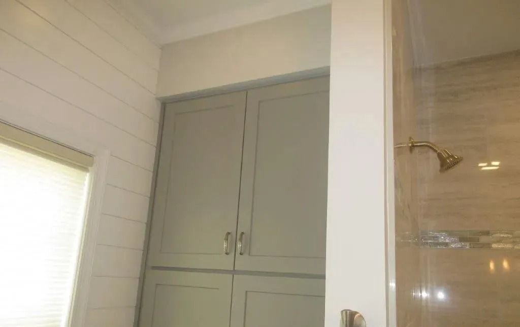 Built-in gray cabinets beside a shower with gold fixtures in a tiled bathroom