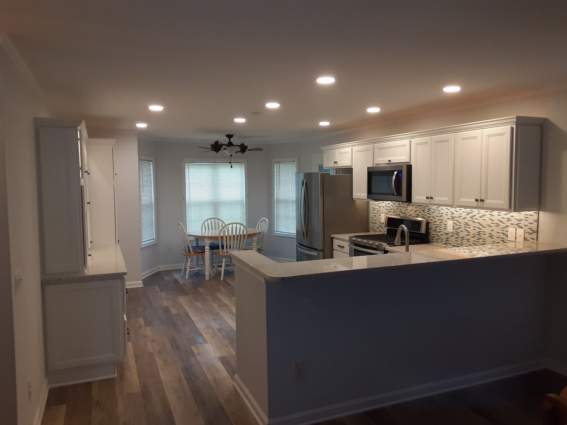 Open kitchen with gray cabinets, white countertops, wood floors, and a dining area by the window.
