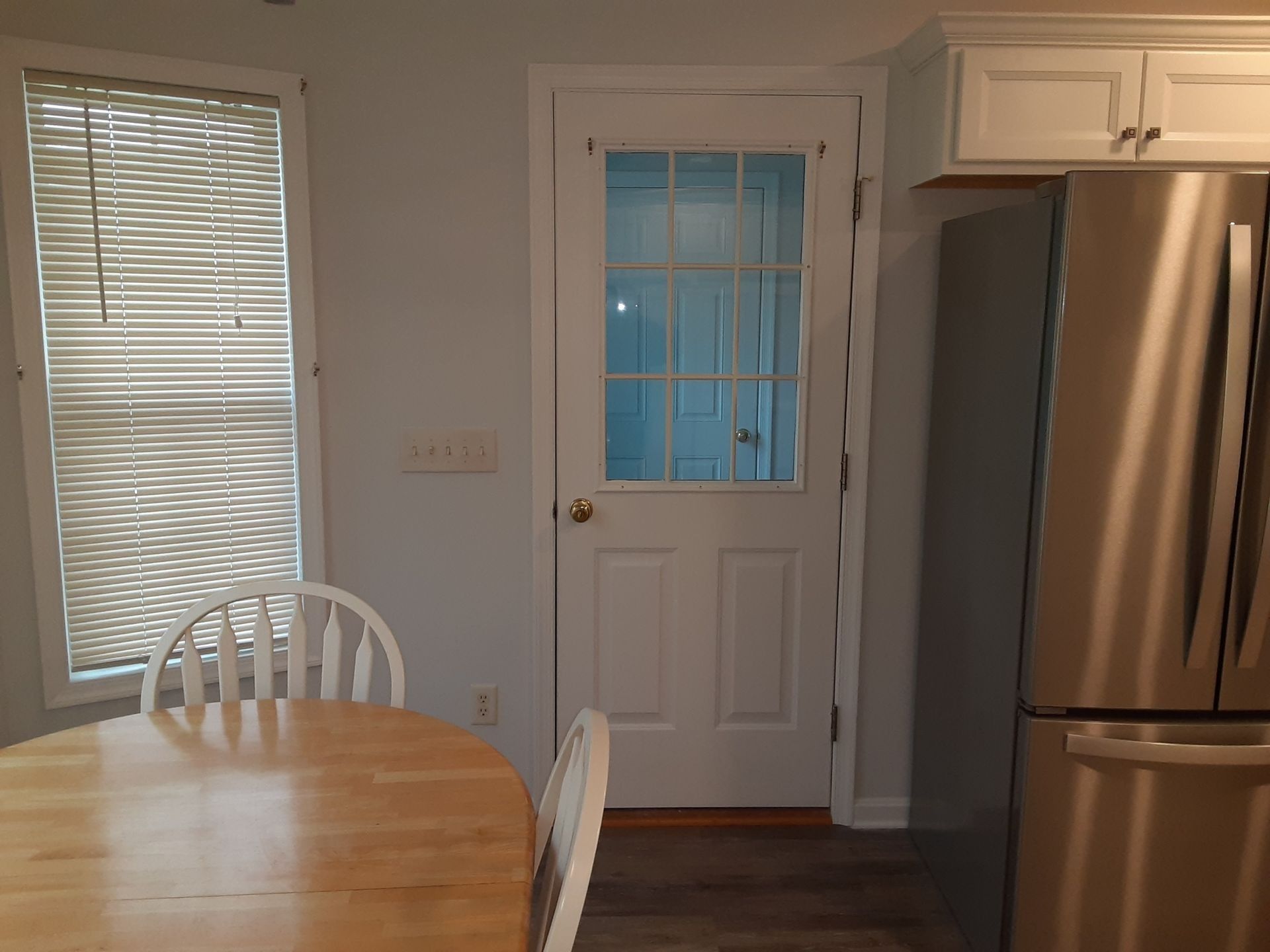 Kitchen with wooden table and chairs, white back door, and stainless steel refrigerator.