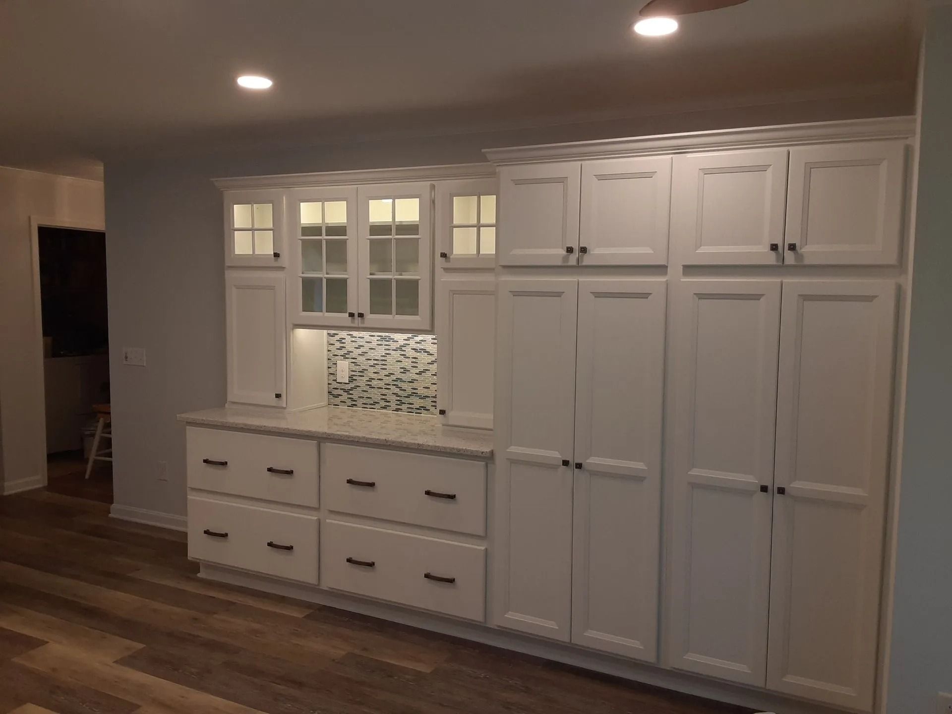 White built-in cabinets and drawers with a tiled backsplash in a softly lit kitchen nook.